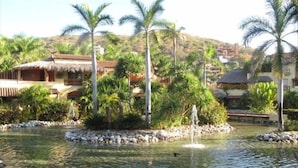A tranquil pond with a fountain, surrounded by palm trees and a small island. - <br>Private beach Exclusive Beach Zihuatanejo, direct access La Ropa RVILLAS SOL (ZIHUATANEJO)