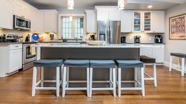 A modern kitchen with white cabinets, stainless steel appliances, a central island with bar stools, and pendant lighting.