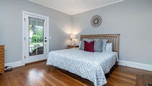 A bedroom with a wooden bed, a nightstand with a lamp, a decorative wall piece, and a door leading outside.