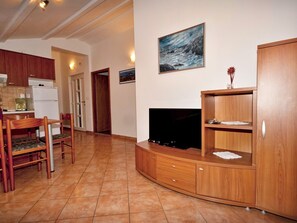 A living room with a TV, wooden cabinets, a dining area with chairs, and a kitchen in the background. - Apartments Snjezana (Medulin)