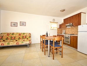 A compact living space with a sofa, dining table, chairs, a kitchen area including a stove and refrigerator, and a clock on the wall. - Apartments Snjezana (Medulin)