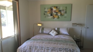 Un dormitorio ordenado con cama, lámparas de noche, un banco y una ventana con cortinas.