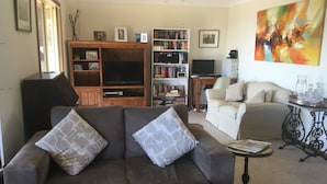 Una sala de estar con un sofá, una mesa de centro, una estantería, un televisor y un cuadro en la pared.