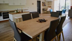 A spacious living area with a wooden dining table surrounded by chairs, a kitchen with white cabinets, and a door leading to another room. - Farm Escape - Spacious Cottage in Kangaroo Valley (Kangaroo Valley)