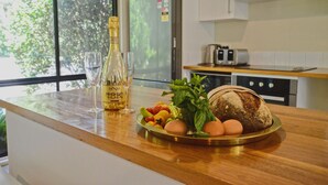 A kitchen counter with a bottle of wine, glasses, a plate of vegetables, eggs, and a loaf of bread. - Farm Escape - Spacious Cottage in Kangaroo Valley (Kangaroo Valley)