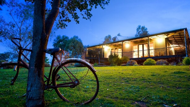 A rustic wooden house with a porch, a bicycle leaning against a tree, and a well-maintained lawn. - Kookaburra Ridge - beautiful home set on a 1.6 acre garden with fireplace & spa (Hepburn)