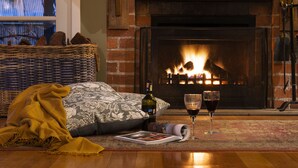 A cozy room with a fireplace, a wicker basket, a blanket, a pillow, a wine bottle, and two wine glasses. - Kookaburra Ridge - beautiful home set on a 1.6 acre garden with fireplace & spa (Hepburn)