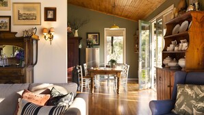 A cozy living room with a wooden dining table, chairs, and a sofa with cushions. - Kookaburra Ridge - beautiful home set on a 1.6 acre garden with fireplace & spa (Hepburn)