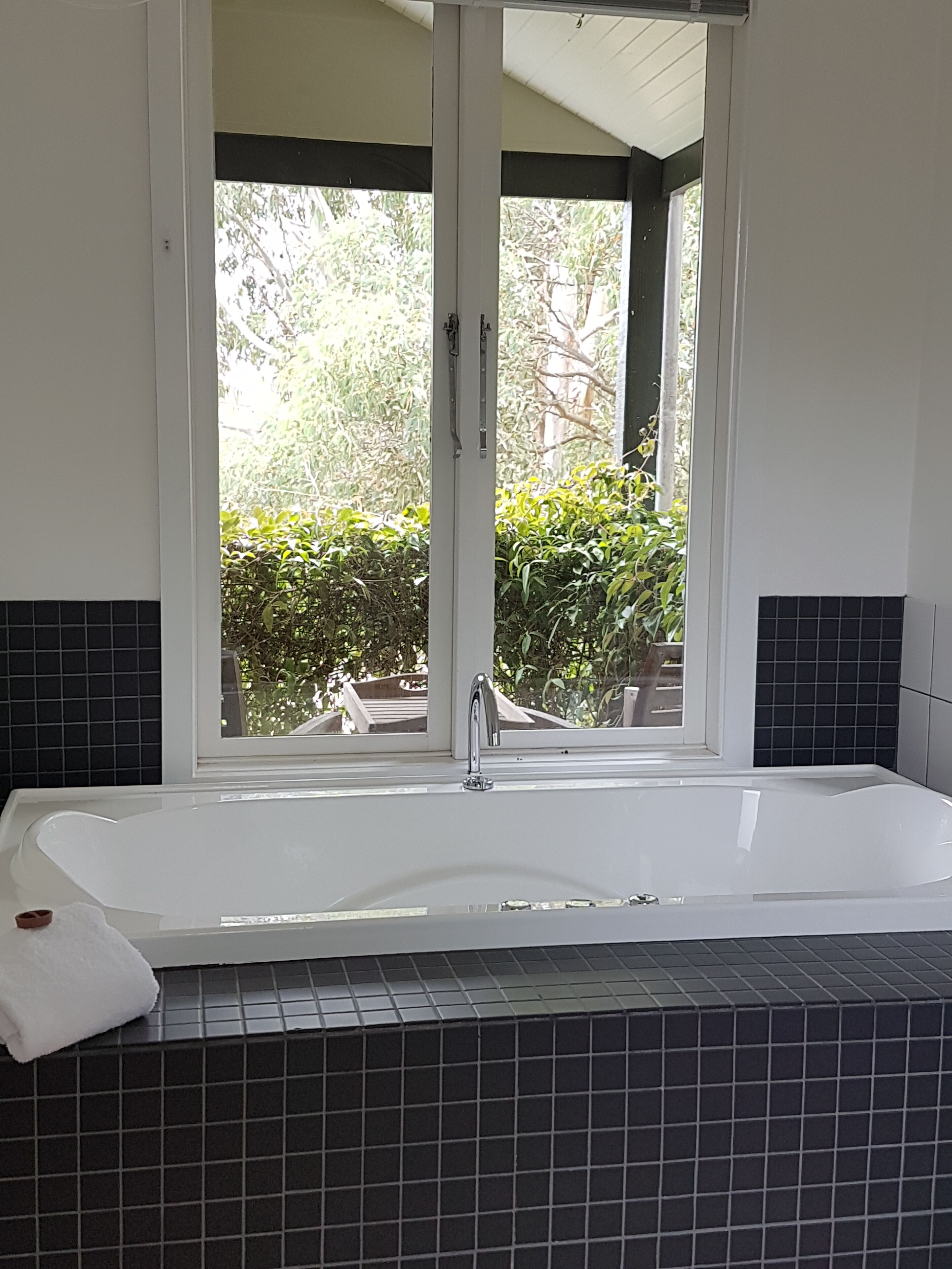 A bathroom with a bathtub, a window, and a view of greenery outside.