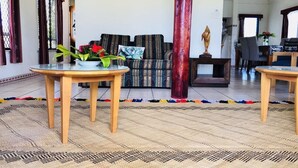 Uma sala de estar com um sofá, duas mesas de madeira, um vaso decorativo e um pilar grande.