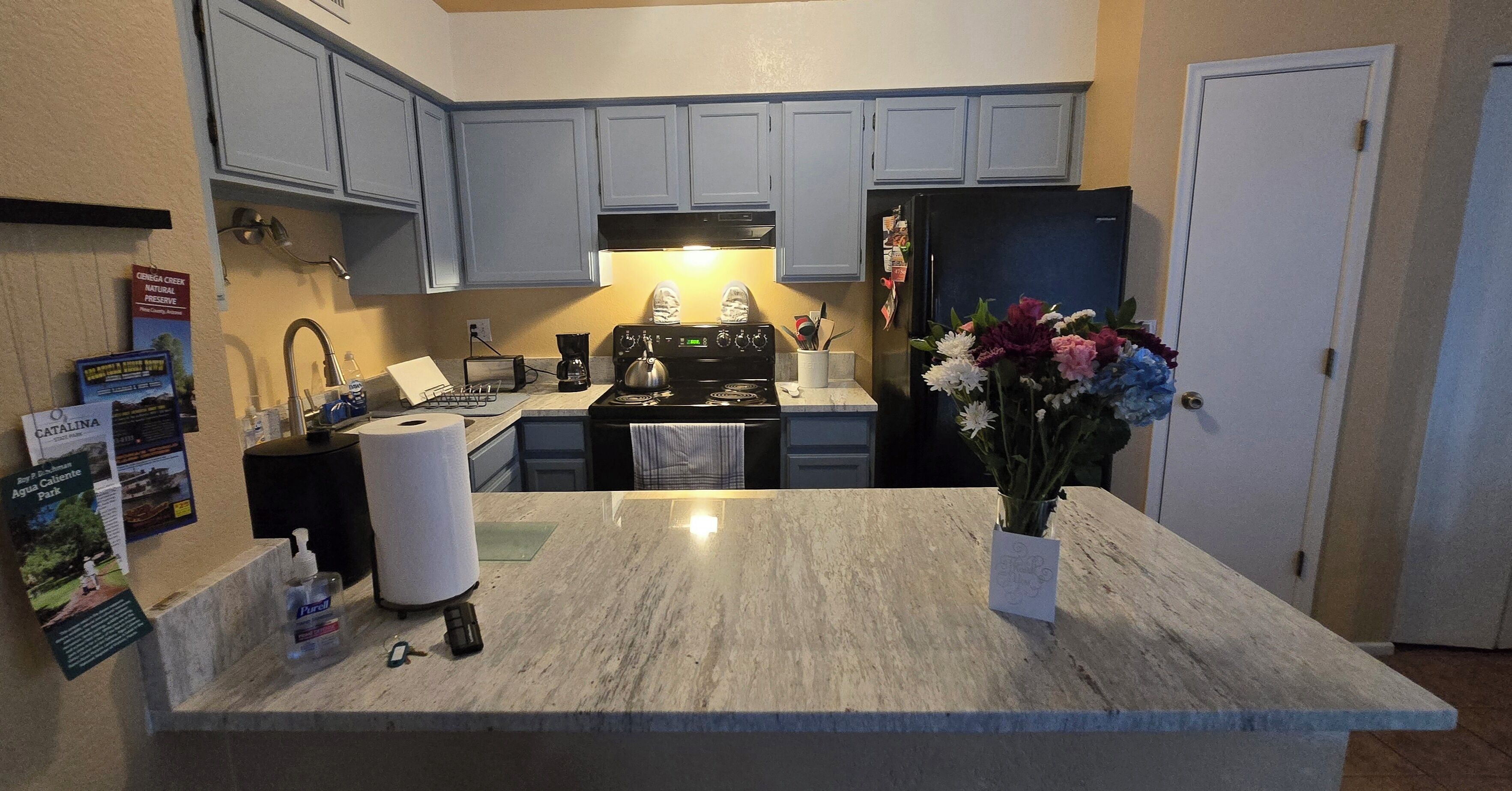 Una cocina con alacenas azul claro, un refrigerador negro, una estufa y una encimera de mármol.