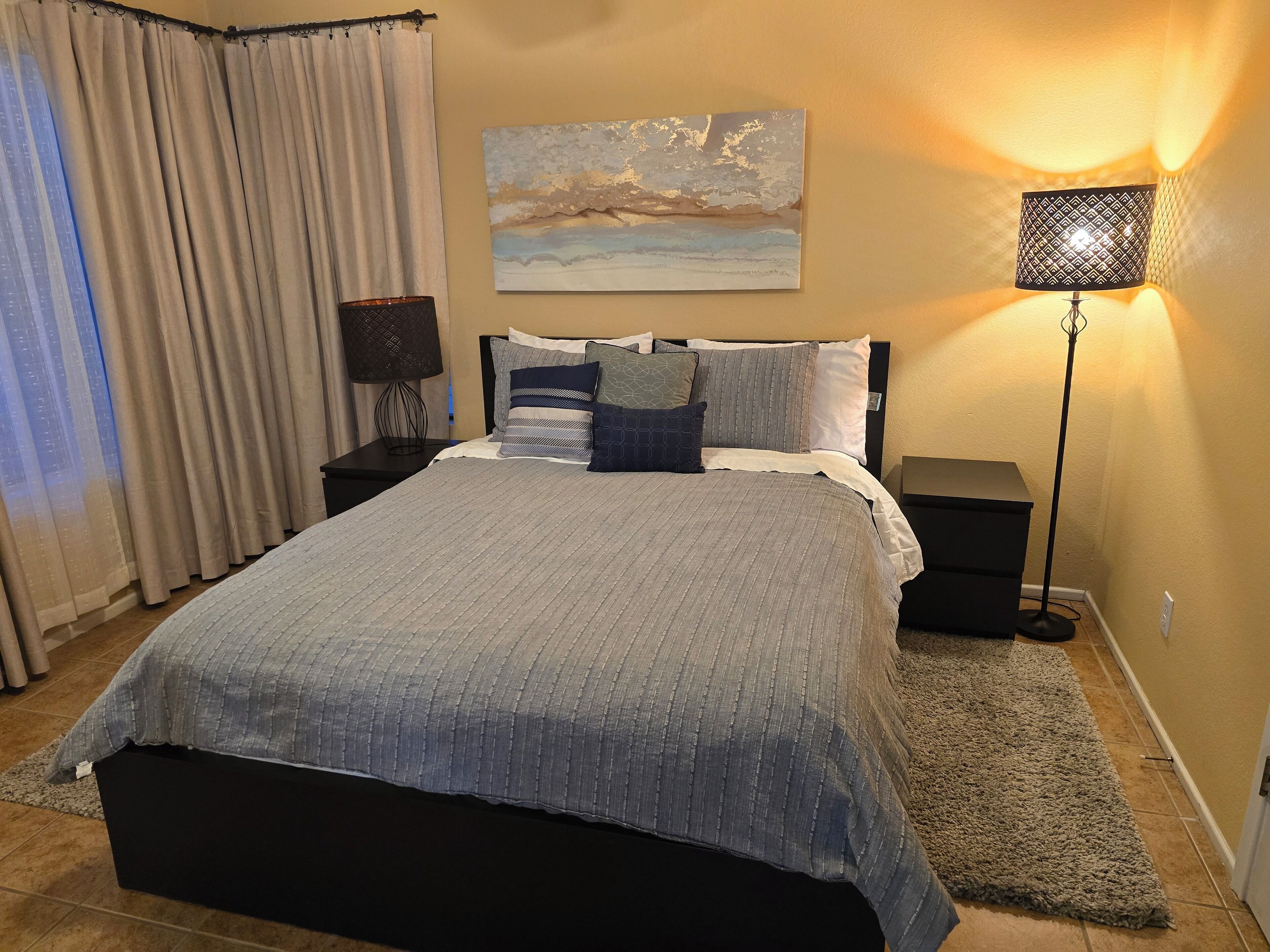 A neatly arranged bedroom with a bed, bedside tables, a lamp, and a painting on the wall.