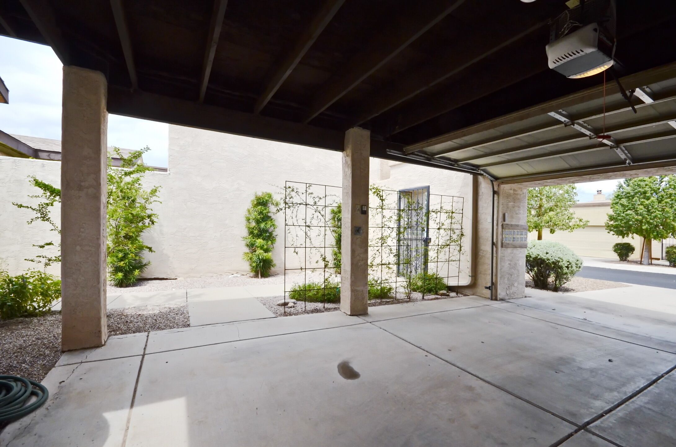 A covered outdoor area with concrete pillars, a metal fence, and greenery.