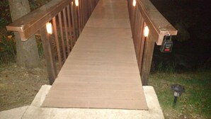 A wooden bridge with railings and lights, leading to a grassy area.