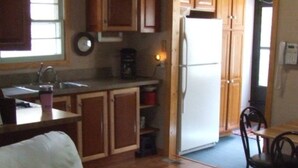 A compact kitchen with wooden cabinets, a refrigerator, a coffee maker, and a dining area with a table and chairs.