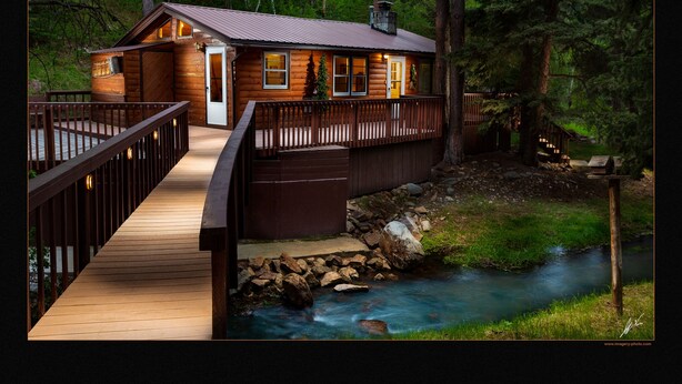 A wooden cabin with a deck and a river in the background.