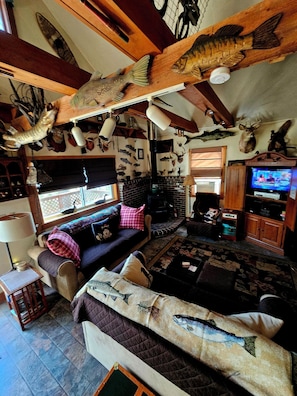 Uma sala de estar aconchegante com lareira, um sofá e diversos peixes e veados montados nas paredes.