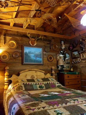 Um quarto rústico de madeira com uma cama, um quadro emoldurado e diversos objetos decorativos, incluindo pratos e chifres.