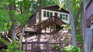 A cabin with a wooden staircase leading to a deck, surrounded by trees. - Sweet By and By... Your Escape to the Beauty of Smith Mountain Lake (Huddleston)