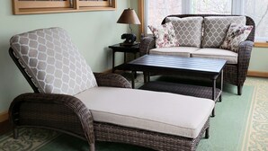A cozy living room with wicker furniture, a patterned armchair, a sofa with floral cushions, and a small table with a lamp. - Sweet By and By... Your Escape to the Beauty of Smith Mountain Lake (Huddleston)