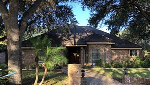 A brick house with a dark roof, a front porch, and a palm tree in the yard.