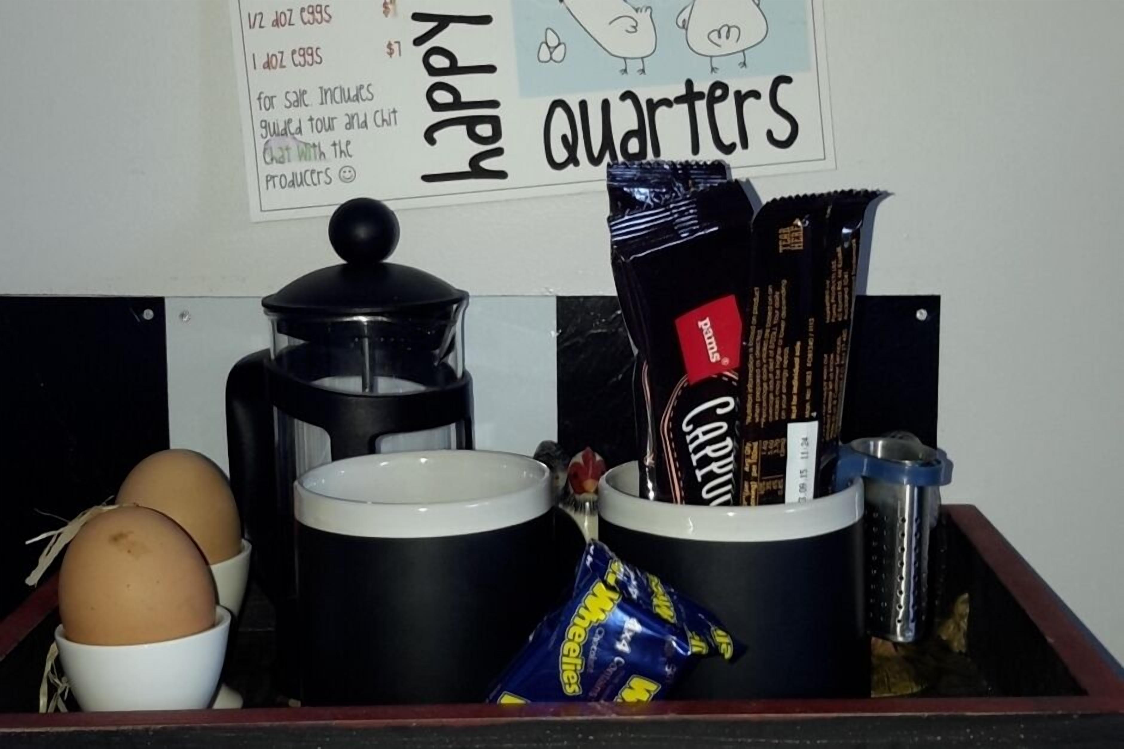A kitchen counter with a coffee maker, a pot, two mugs, eggs, chocolate bars, and a packet of snacks.