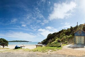 A beach scene with a small wooden building, a bench, and a tent. - Four Seasons in one Day (Oneroa)