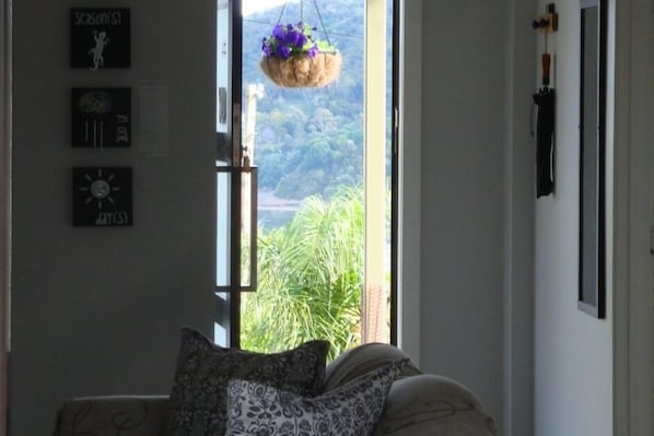 A room with a bed, a window with a view of greenery, and wall-mounted clocks. - Four Seasons in one Day (Oneroa)