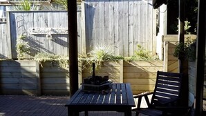 Une terrasse en bois avec une table et des chaises, entourée d’une clôture en bois et agrémentée de quelques plantes.