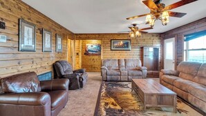 A log cabin interior with leather sofas, a wooden coffee table, ceiling fans, framed pictures, and a fireplace. - Reel'em In Lodge - A Reel Fisherman Lodge! (St Bernard)