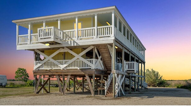 A two-story wooden structure with balconies, elevated on stilts, and a clear sky in the background. - Reel'em In Lodge - A Reel Fisherman Lodge! (St Bernard)