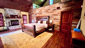 Ein Schlafzimmer mit Kamin aus Stein, Holzwänden, einem großen Bett und einer Holzbank.