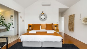 A modern bedroom with a large bed, two bedside tables with lamps, a wall-mounted mirror, and a hanging woven tapestry. - EAST COAST ESCAPES | Lighthouse Studio (Byron Bay)