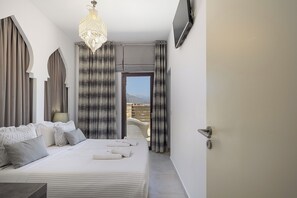 A modern hotel room with a large bed, a chandelier, and a view of the mountains. - Private Beachfront Estate located on the beach of Paralia Kournas (Rethymno)