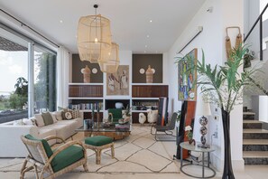 A modern living room with a sofa, chairs, a coffee table, and a bookshelf. - Villa Amnalys - Sea View, Gardens & Spa by etouri (Rethymno)
