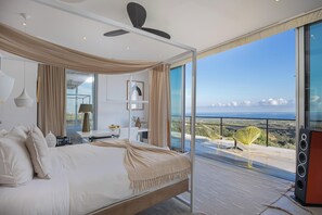 A bedroom with a large bed, a ceiling fan, and a view of the sea through a sliding glass door. - Villa Amnalys - Sea View, Gardens & Spa by etouri (Rethymno)