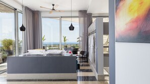 Un dormitorio moderno con una cama grande, un ventilador de techo y vista al océano.