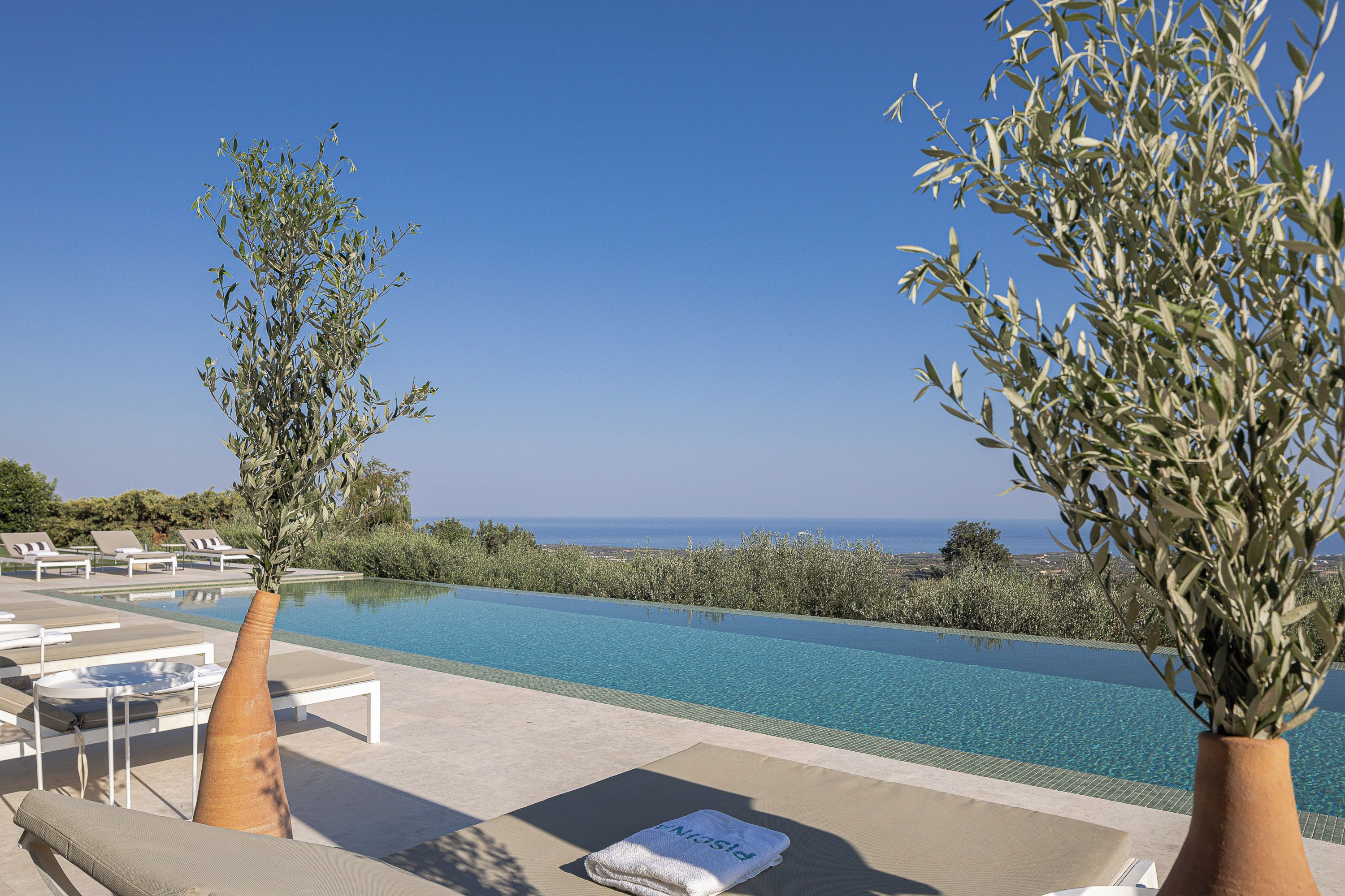 Ein Infinity-Pool mit freiem Blick auf das Meer, umgeben von Liegestühlen und Olivenbäumen.