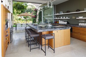 A modern kitchen with a central island, bar stools, and a view of a lush garden.