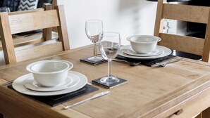 Uma mesa de jantar de madeira posta com tigelas, pratos, uma taça de vinho e talheres brancos.