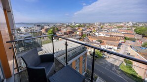 A balcony with wicker chairs, a glass railing, and a city view. - Tides - Poole Town Views, On-site Parking (Poole)