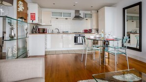 A modern kitchen with white cabinets, a glass dining table, and clear chairs. - Tides - Poole Town Views, On-site Parking (Poole)