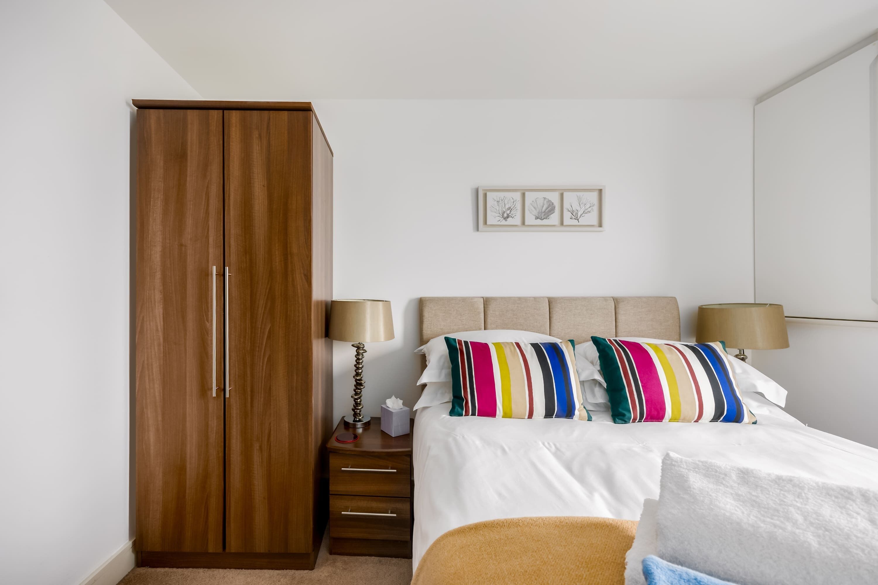 Une chambre avec une armoire en bois, un lit avec des oreillers à rayures, des lampes de chevet et un tableau encadré au mur.