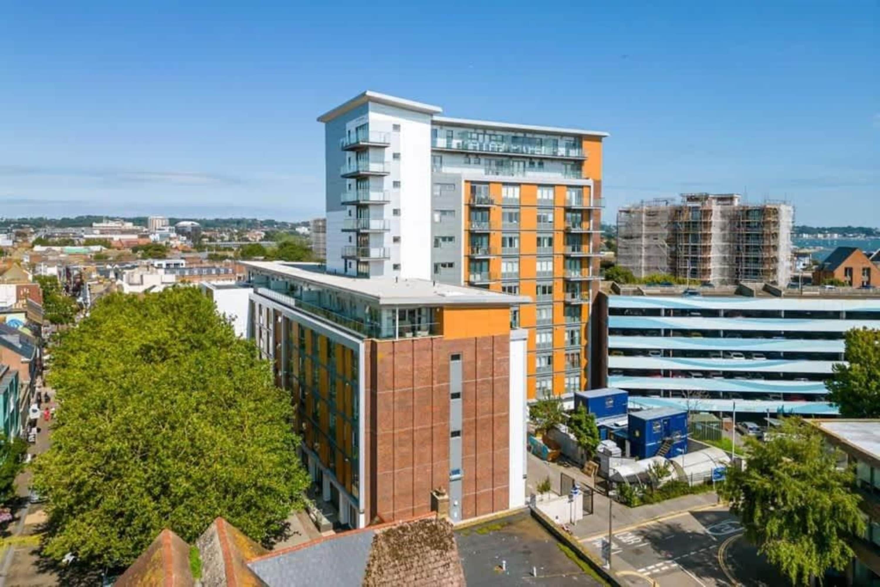 Un immeuble à plusieurs étages, doté d’une architecture moderne, avec une façade combinant verre et briques, et un espace de stationnement situé à l’avant.