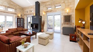 A spacious living room with a fireplace, a sofa set, a coffee table, and a dining area with a wooden table and chairs. - Spacious villa with full privacy & nature views! (Rethymno)