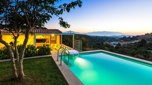 A swimming pool with a view of mountains, a covered outdoor seating area, and a well-maintained lawn. - Spacious villa with full privacy & nature views! (Rethymno)
