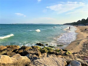 Una spiaggia con un primo piano roccioso, acqua cristallina e una battigia sabbiosa.