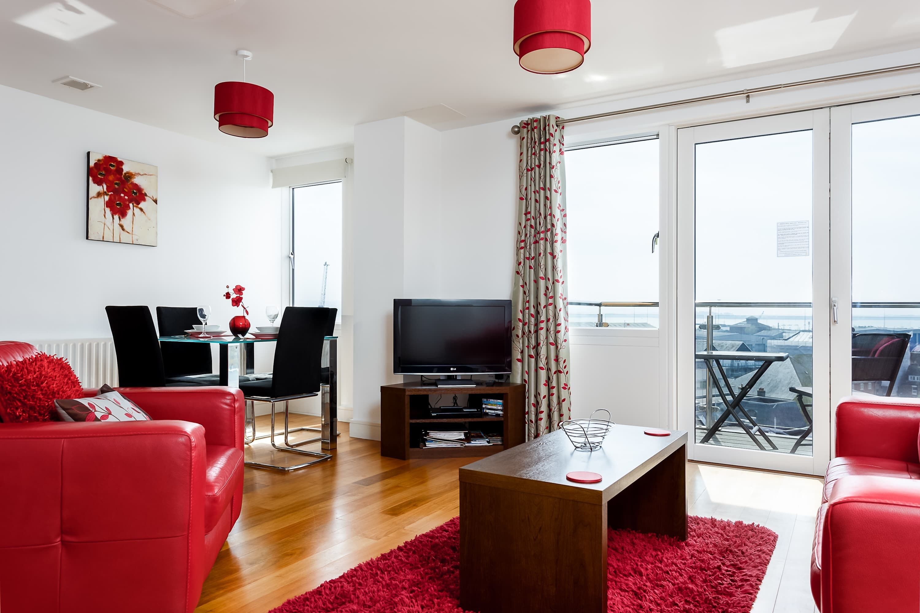 Un salon moderne avec des meubles rouges, un téléviseur à écran plat et un coin repas comprenant une table et des chaises.