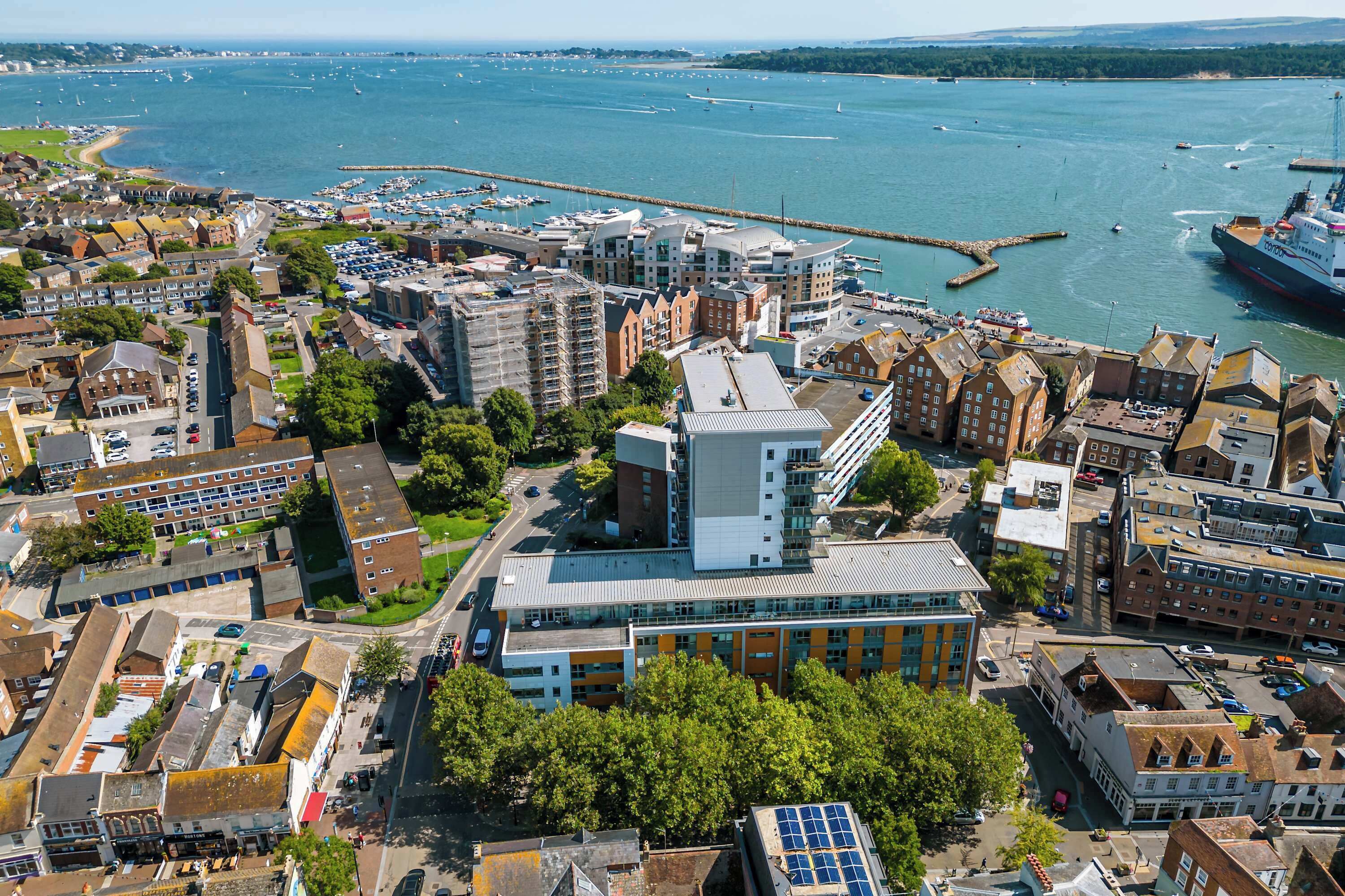 An aerial view of a coastal city with modern and historic buildings, a marina, and a large cruise ship docked.