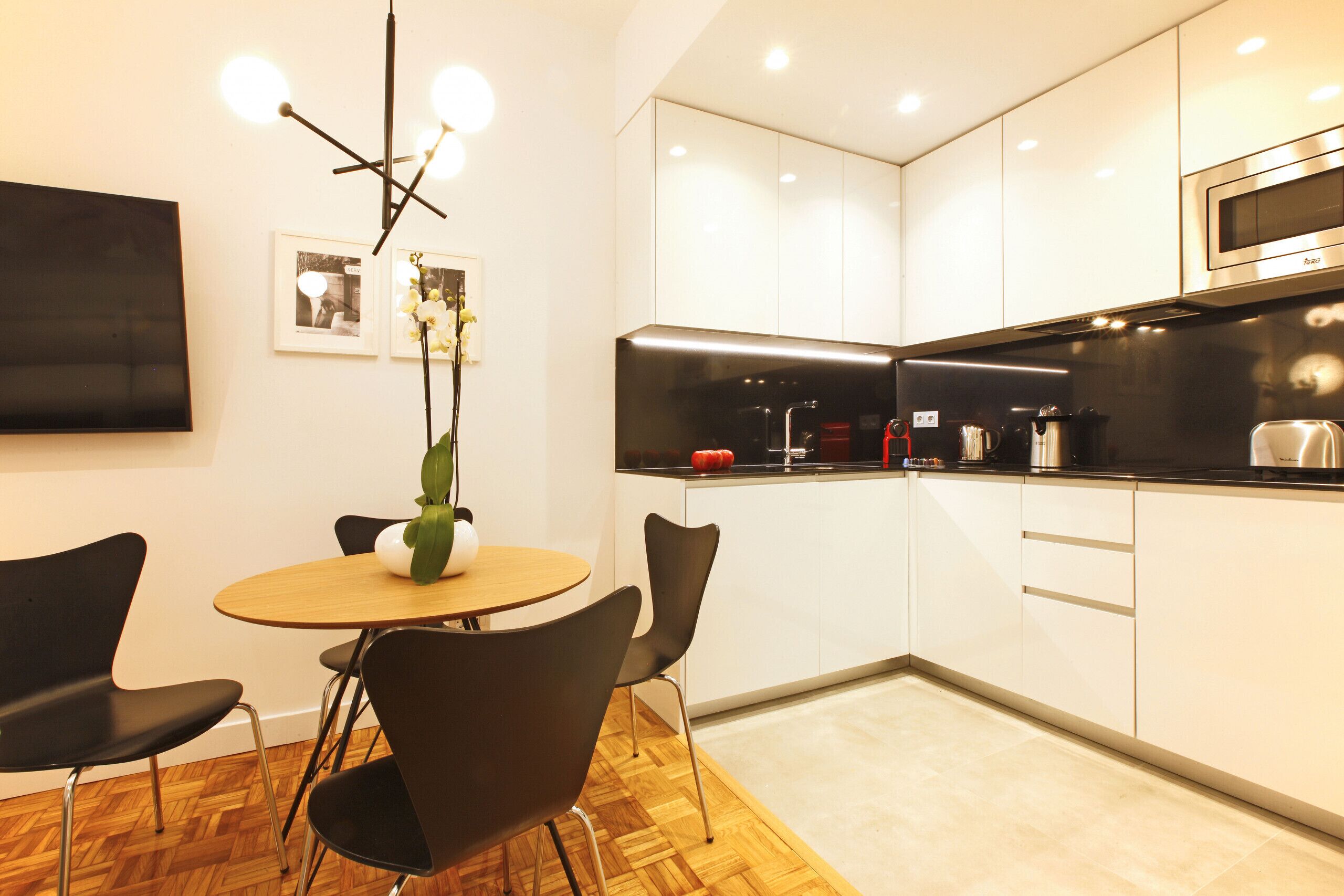 A modern kitchen with white cabinets, a black countertop, and a round wooden table with black chairs.